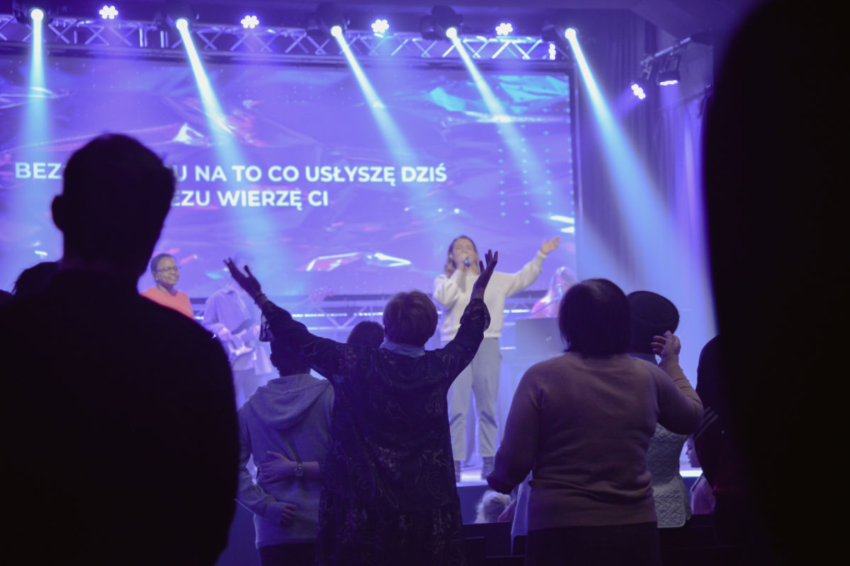 The congregation sings with raised hands in front of a stage lit in blue