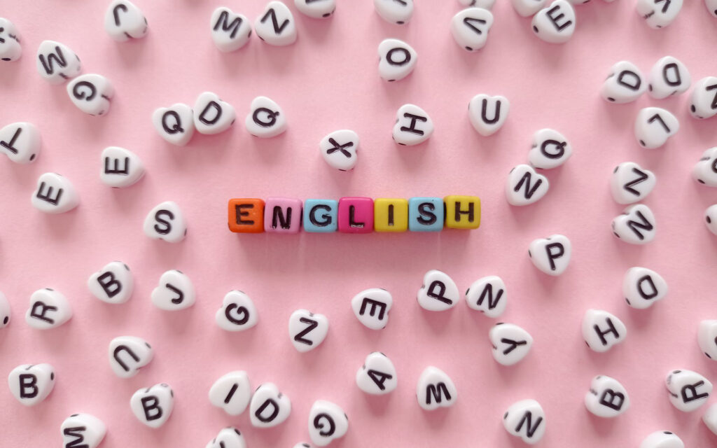 Kolorowe koraliki z literami układają się w słowo ENGLISH na różowym tle
