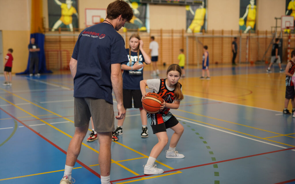 Trener pokazuje dziewczynce z piłką ćwiczenie na treningu koszykówki w hali sportowej